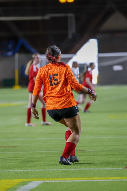 Soccer player striking the ball in an orange training vest
